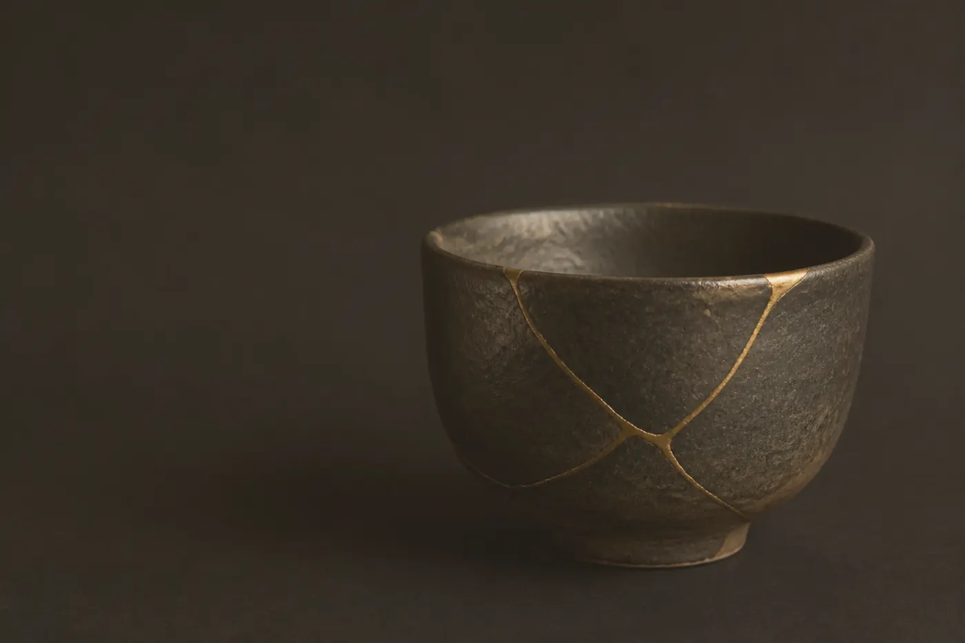 Ciotola in ceramica scura riparata con vene d’oro, tecnica kintsugi, su fondo inchiostro (immagine concettuale)